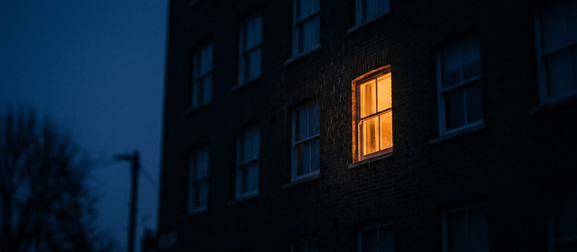 Een verlicht raam in de schemering, eenzaamheid als signaal